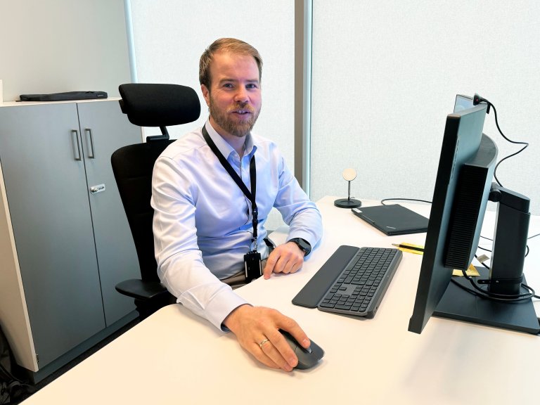 Portrettbilde av Andres Neset, sitter ved pult foran datamaskin
