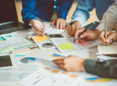 Mennesker som team jobbe sammen, hender holder blyanter og peker på papir som ligger på bordet, utsnittet er av armer og hender.