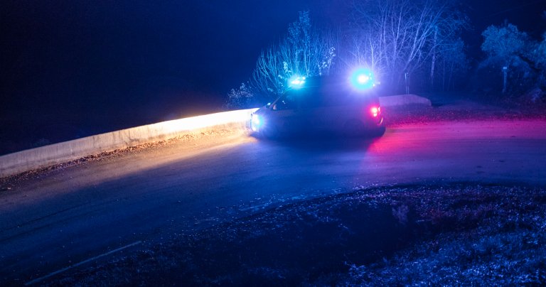 Ambulanse med blålys står parkert på veien, i en sving, det er natt