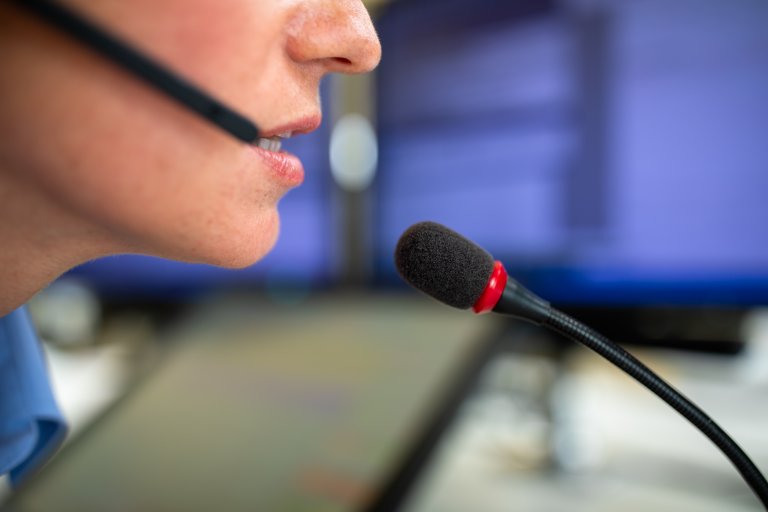 Nærbilde av telefonoperatør, nærbilde av munn som snakker i mikrofon, deler av headset synlig langs kinn