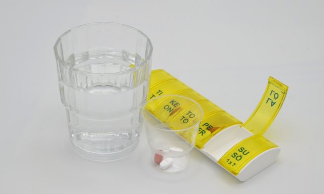 Vannglass, pilledosering, piller i ulike farger og fasonger ligger oppi plastkopp og dosett