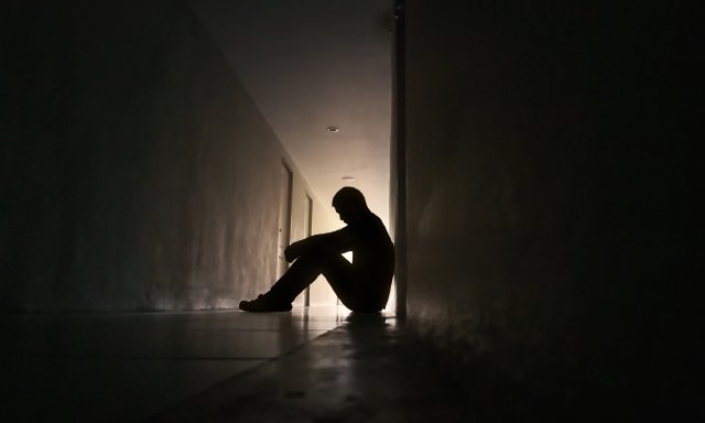 Mann sitter på gulvet med armene på knærne og hodet ned i en lang mørk gang.