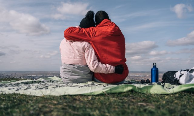 Par som holder rundt og lener hodene mot hverandre,  sitter ute, rygger mot kamera