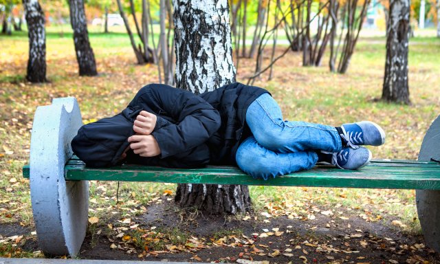 Ung mann ligger på en benk i en park