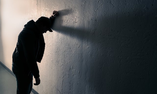 Mann stående mot vegg, støtter seg til armen mot veggen